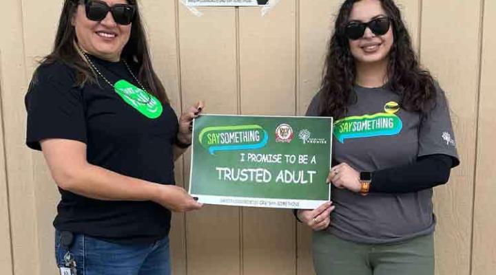 Two women with sunglasses smiling holding sign